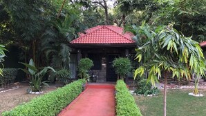 Un chemin menant à un bâtiment surmonté d’un toit rouge, entouré de haies soigneusement taillées et de diverses plantes.