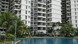 A modern high-rise residential building with a swimming pool and lounge chairs. - Favoured Seaview Suite (Johor Bahru)