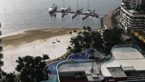 A marina with boats docked, a sandy beach, and a pool area with palm trees. - Favoured Seaview Suite (Johor Bahru)