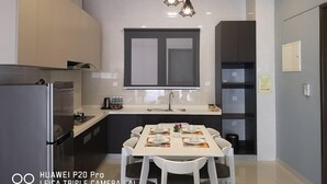 A modern kitchen with a dining area, featuring a large window, a refrigerator, and a table set for four. - Favoured Seaview Suite (Johor Bahru)