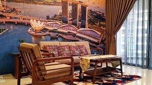 A room with a large mural of a bridge and lotus flowers, a sofa, a wooden chair, a small table, and a patterned rug. - Favoured Seaview Suite (Johor Bahru)