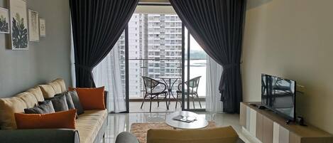A modern living room with a sofa, armchairs, a TV, and a balcony with a view of high-rise buildings.