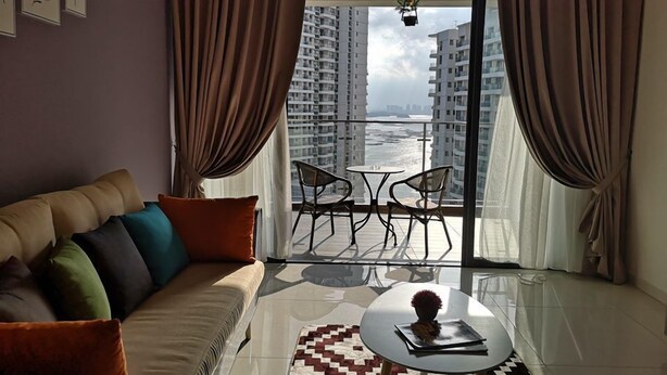 A modern living room with a sofa, a coffee table, and a view of high-rise buildings and a body of water. - Favoured Seaview Suite (Johor Bahru)