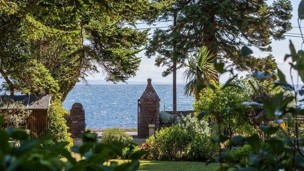 Un jardín costero con estructuras de piedra, abundante vegetación y vistas al mar.
