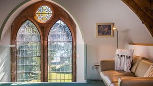 Una habitación con techo de madera, alfombra verde, sofá de cuero y una ventana de vitral.
