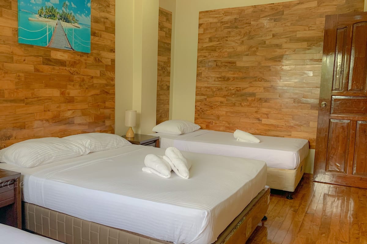 A hotel room with a wooden wall, two beds, a nightstand with a lamp, and a painting of a beach scene.