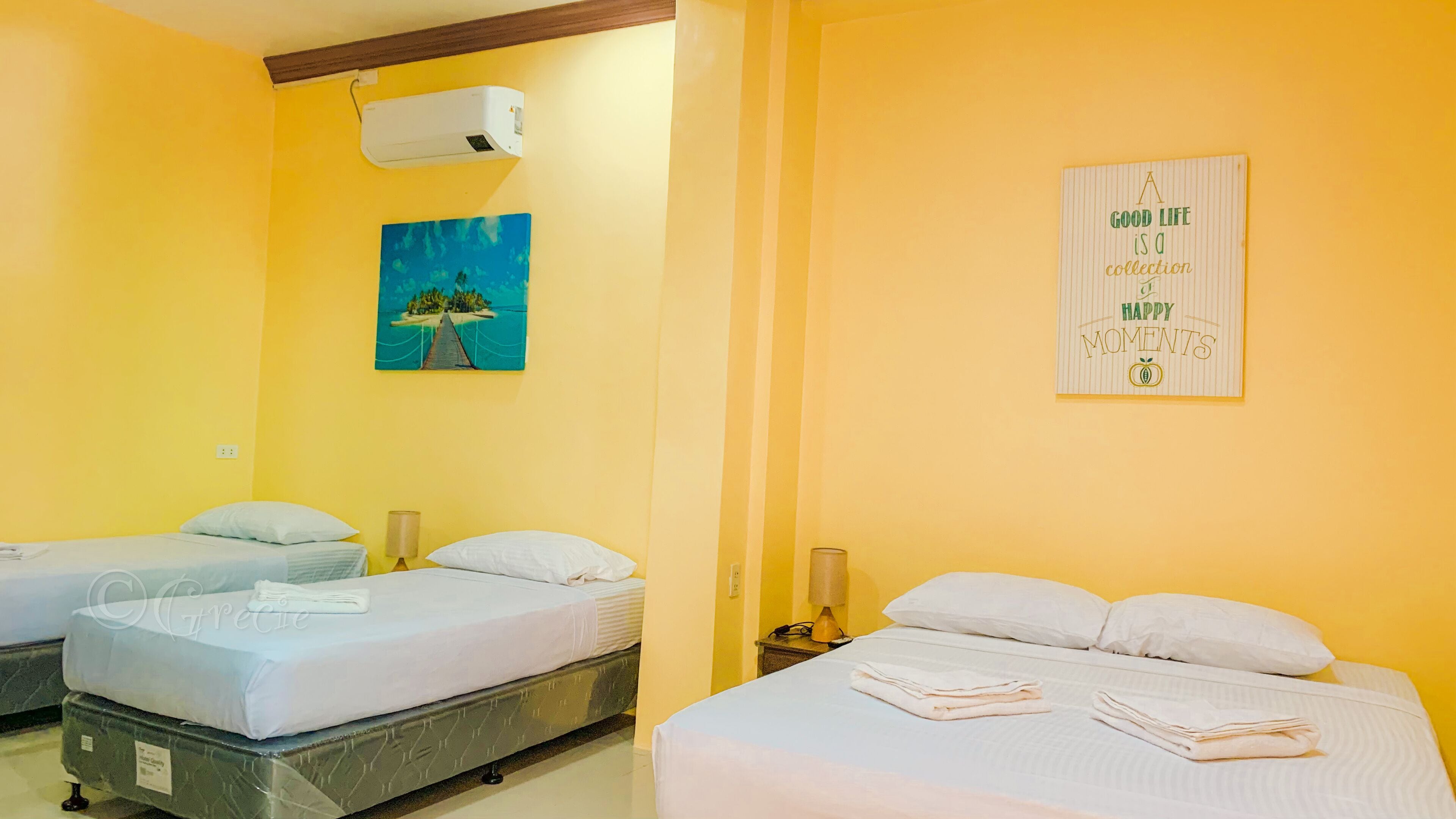 A hotel room with two beds, a painting of a beach scene, an air conditioning unit, and a poster on the wall.