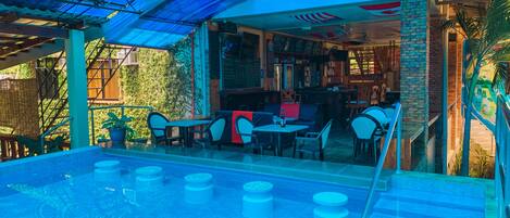 Area piscina all'aperto con posti a sedere e un bar.