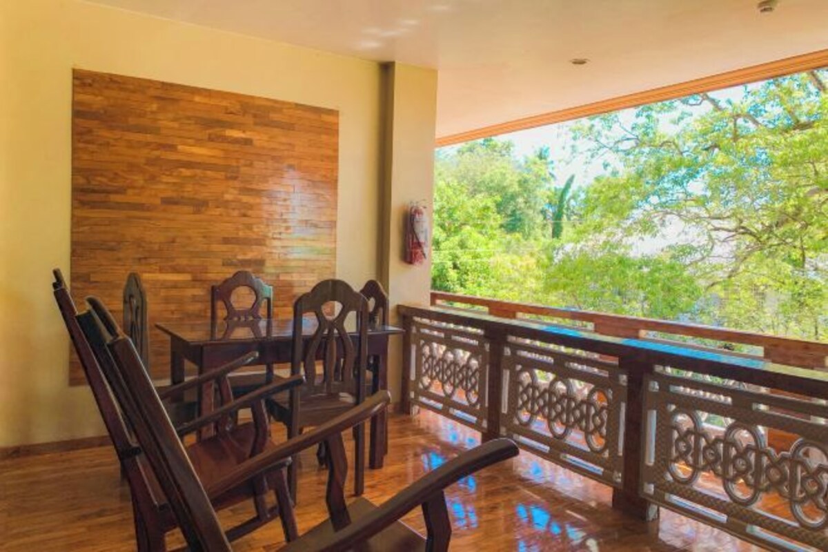 Un comedor de madera con sillas y una mesa, una pared de madera y un balcón con barandilla que da a zonas verdes.