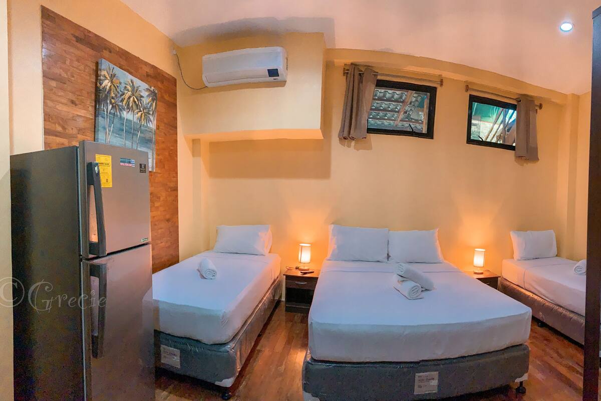 A hotel room with two beds, a refrigerator, an air conditioner, and a window with curtains.