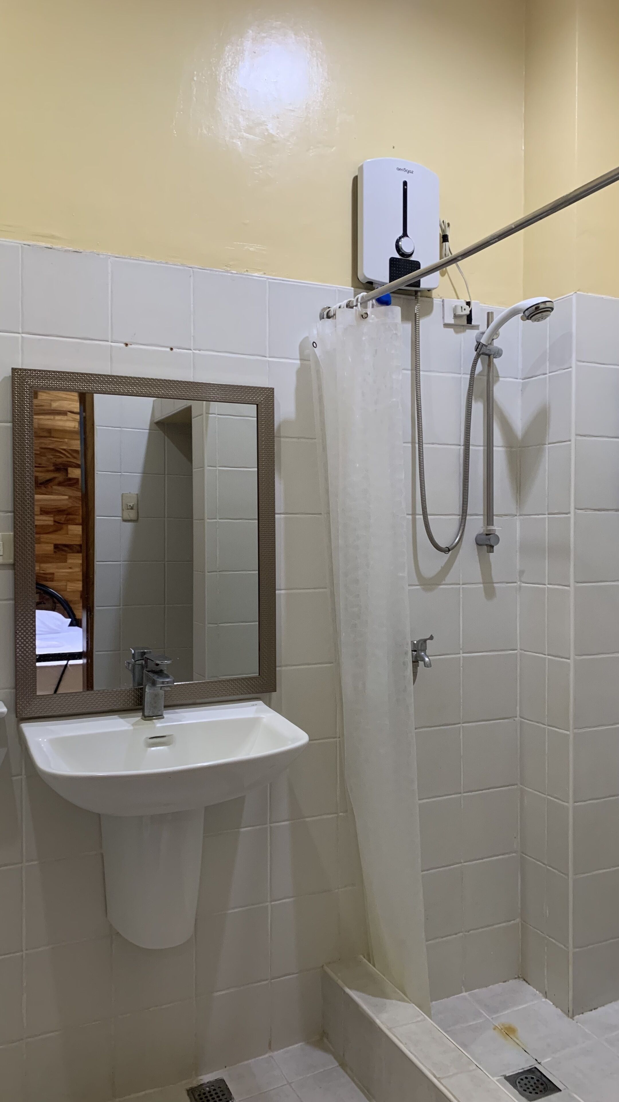 A bathroom with a white sink, a mirror with a wooden frame, a shower with a curtain, and a handheld showerhead.