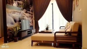 A living room with a sofa, a TV, a plant, and a wall mural. - Garden View Suites (Johor Bahru)