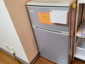 Un frigorifero compatto con un biglietto attaccato, una presa elettrica e un cavo collegato.
