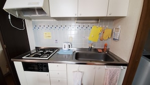 A compact kitchen with white cabinets, a stainless steel sink, a kettle, and a stove. - Petit Asahi 201 (Kobe)