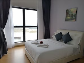 A hotel room with a large window, a bed with white bedding, two pillows, and a painting on the wall. - Picturesque View Suites (Johor Bahru)