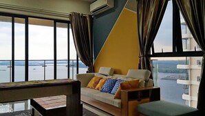 A living room with a sofa, a coffee table, and a view of a body of water through large windows. - Picturesque View Suites (Johor Bahru)