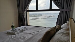 A hotel room with a large window offering a view of a body of water and distant land. - Picturesque View Suites (Johor Bahru)