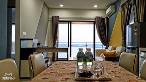 A dining area with a table set for two, a refrigerator, and a view of the sea. - Picturesque View Suites (Johor Bahru)