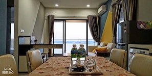 A dining area with a table set for two, a refrigerator, and a view of the sea.