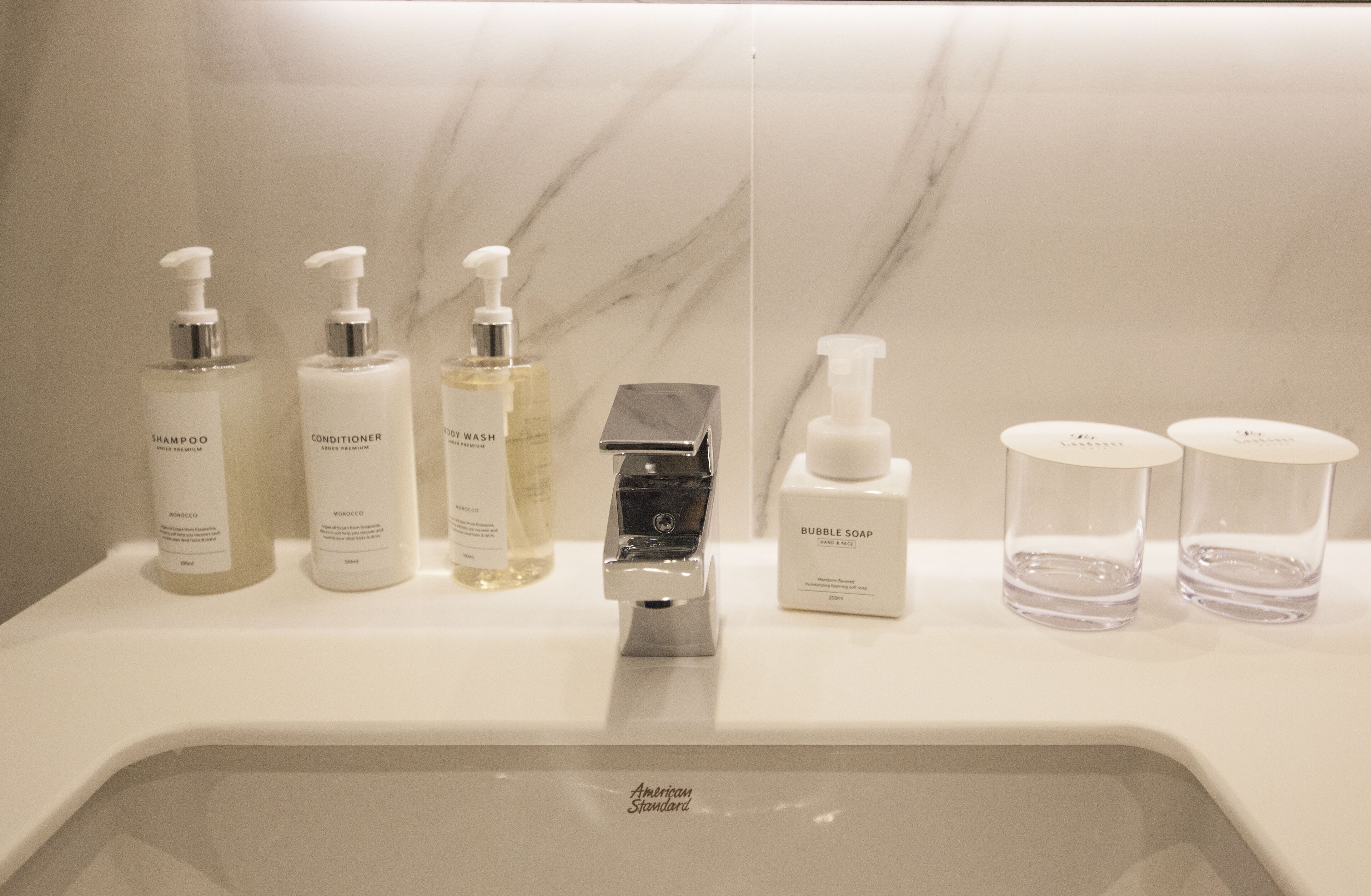 Casa de banho com lavatório de mármore, diversos produtos de higiene pessoal, incluindo shampoo, condicionador e gel de banho, e uma torneira.