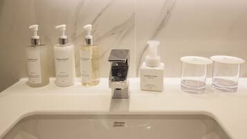 Casa de banho com lavatório de mármore, diversos produtos de higiene pessoal, incluindo shampoo, condicionador e gel de banho, e uma torneira.