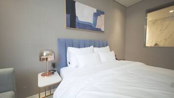 A modern hotel room with a large bed, a bedside table with a lamp, a chair, and a painting on the wall.