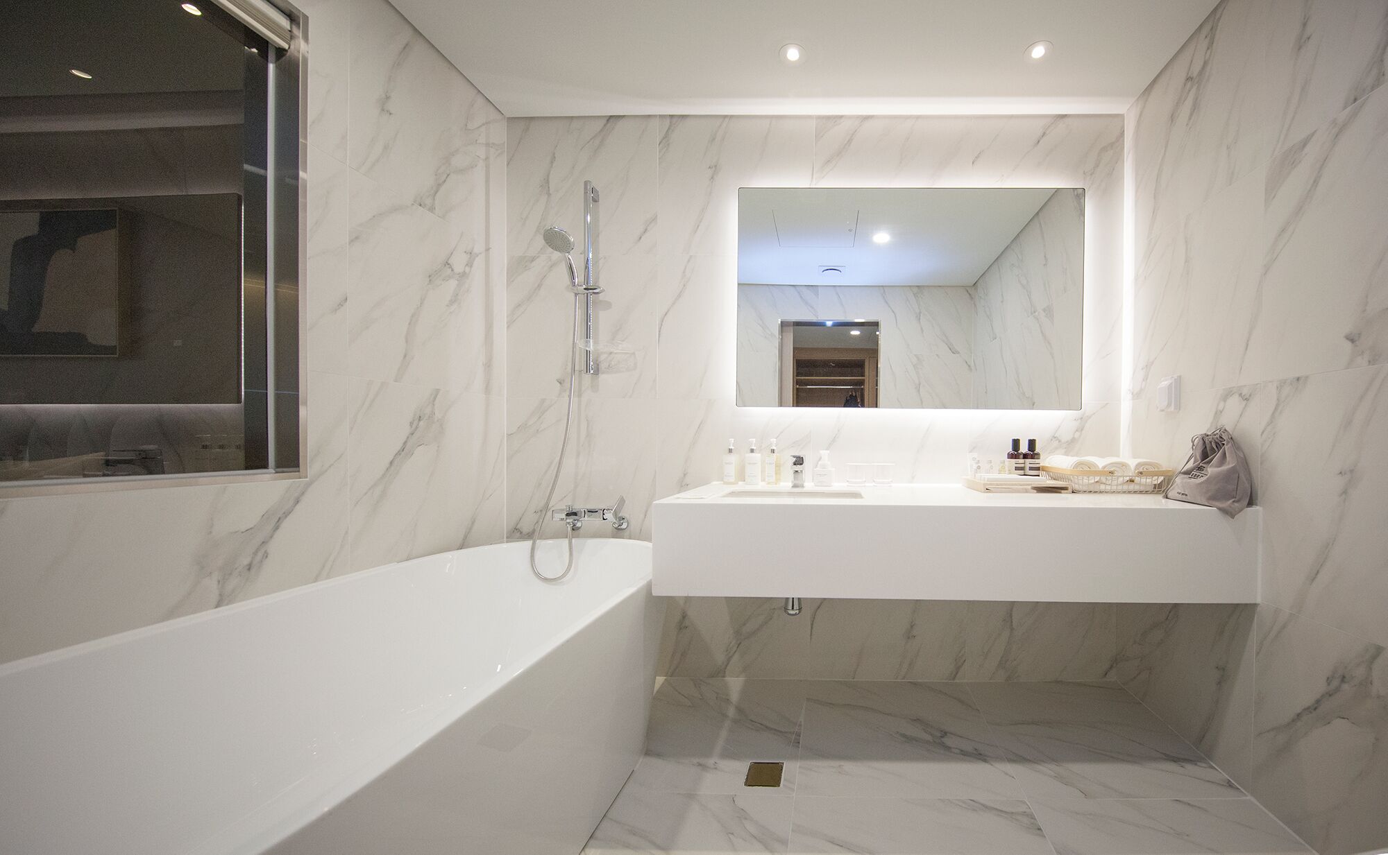 Un baño moderno con una bañera independiente, un espejo grande y un mueble de tocador con artículos de aseo.