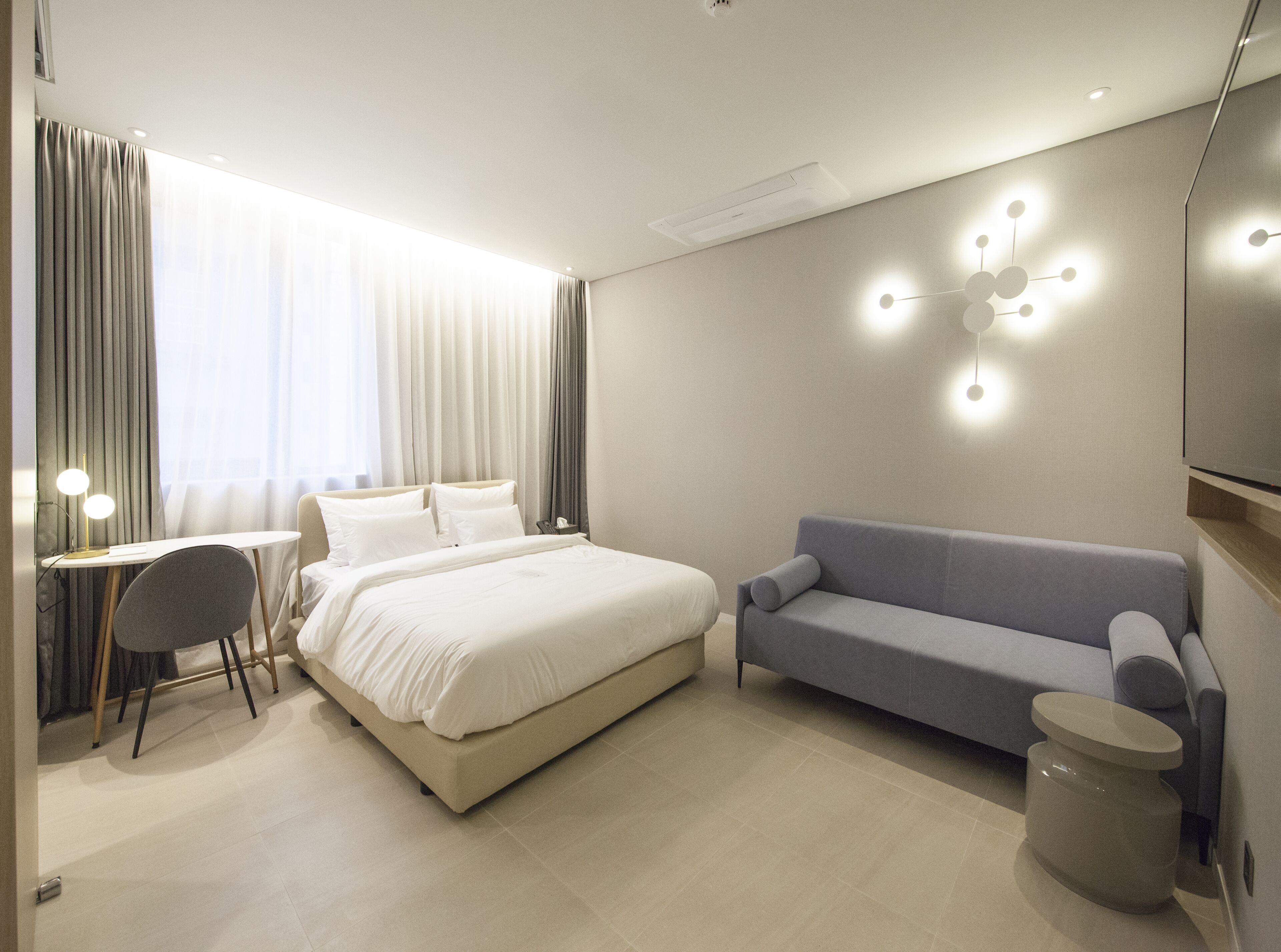 A modern hotel room with a large bed, a sofa, a desk, and a TV.