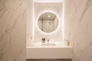 A bathroom with a marble floor, a white sink with a mirror above it, and toiletries on the sink.