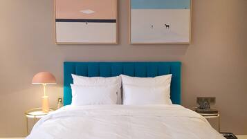 A hotel room with a large bed, a blue headboard, two framed artworks on the wall, a bedside lamp, and a phone on the nightstand.
