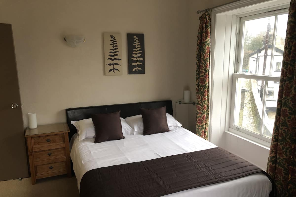 A neatly made bed with a dark headboard, a wooden nightstand with a lamp, and two wall-mounted wall art pieces.