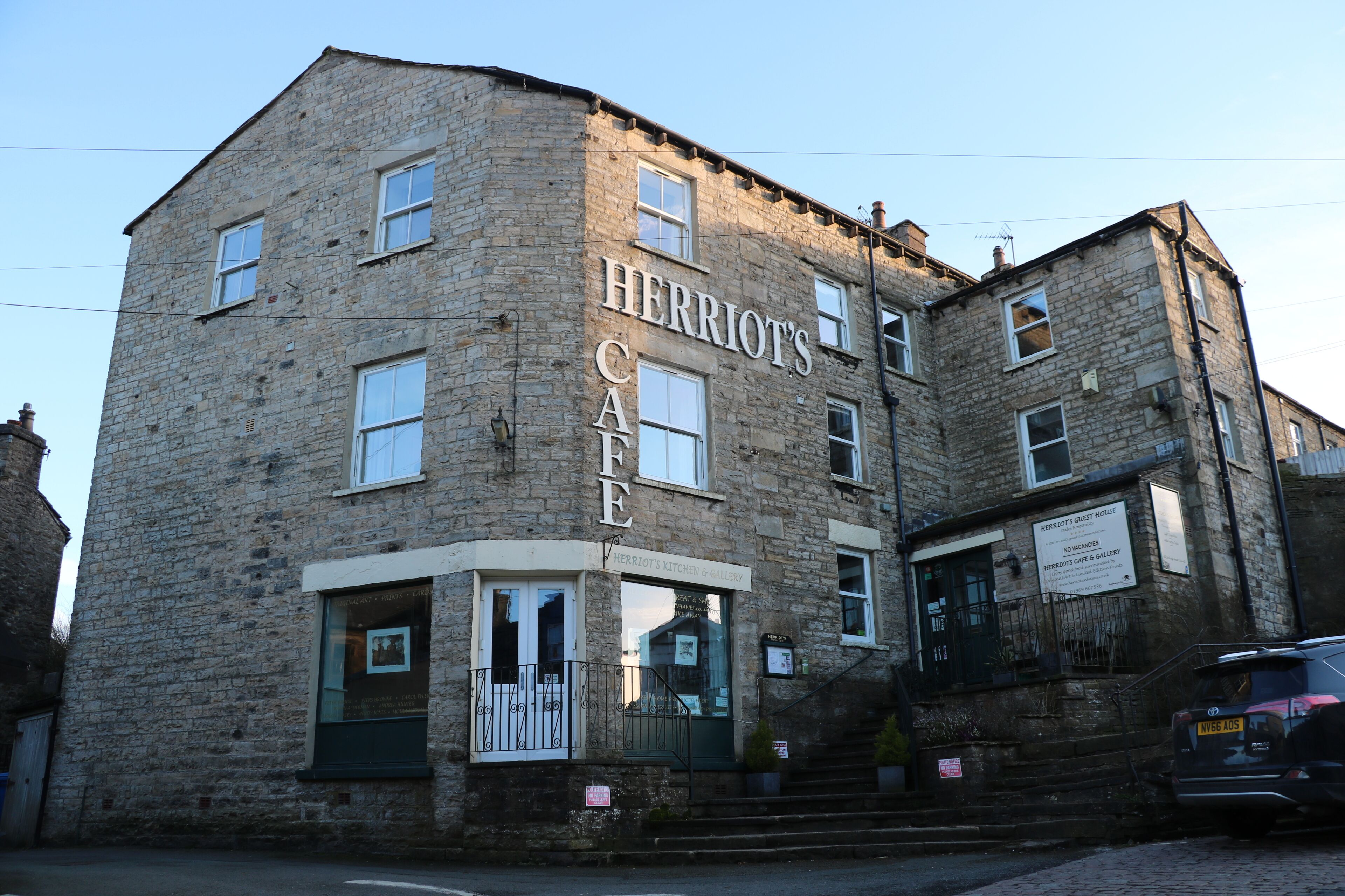 Un edificio de piedra con un cartel que dice 'HERRIOT'S CAFE' y un cartel más pequeño que anuncia 'HERRIOT'S KITCHEN & GALLERY'.
