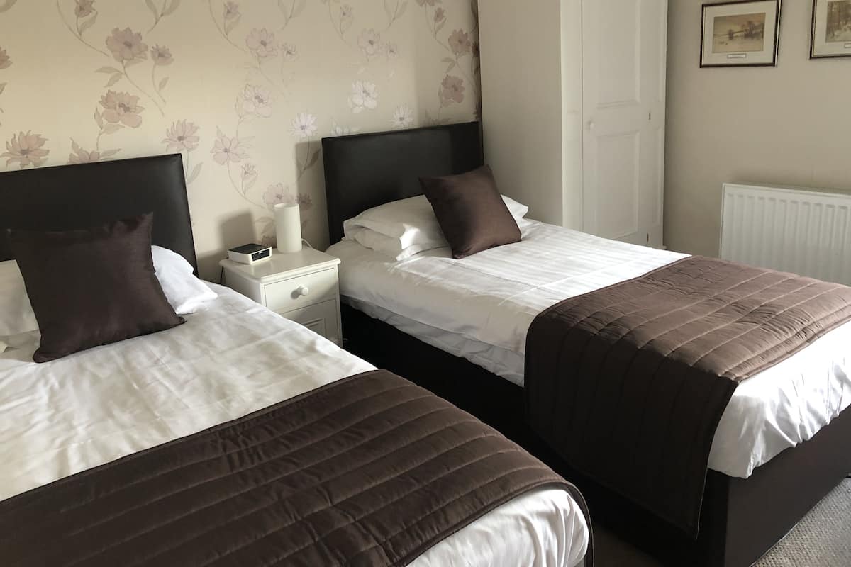 A hotel room with two beds, a nightstand, a white wardrobe, and floral wallpaper.