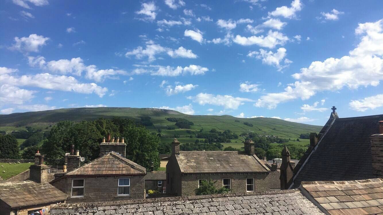 A rural landscape with traditional stone buildings, a clear sky, and rolling hills in the distance.
