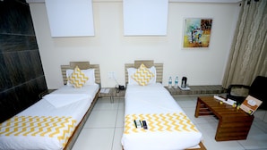 A hotel room with two beds, a wooden nightstand, a desk, and a chair. - Hotel darshan naroda (Ahmedabad)