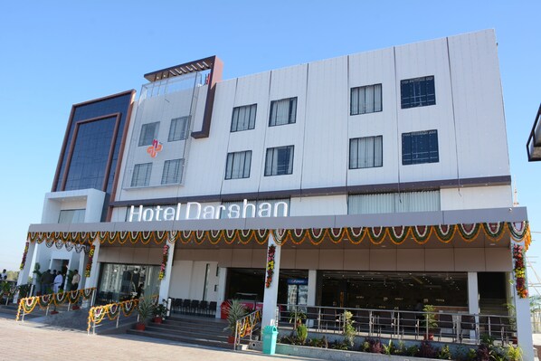 Un hotel llamado "Hotel Darshan" con una fachada moderna, múltiples ventanas y una entrada bien decorada.
