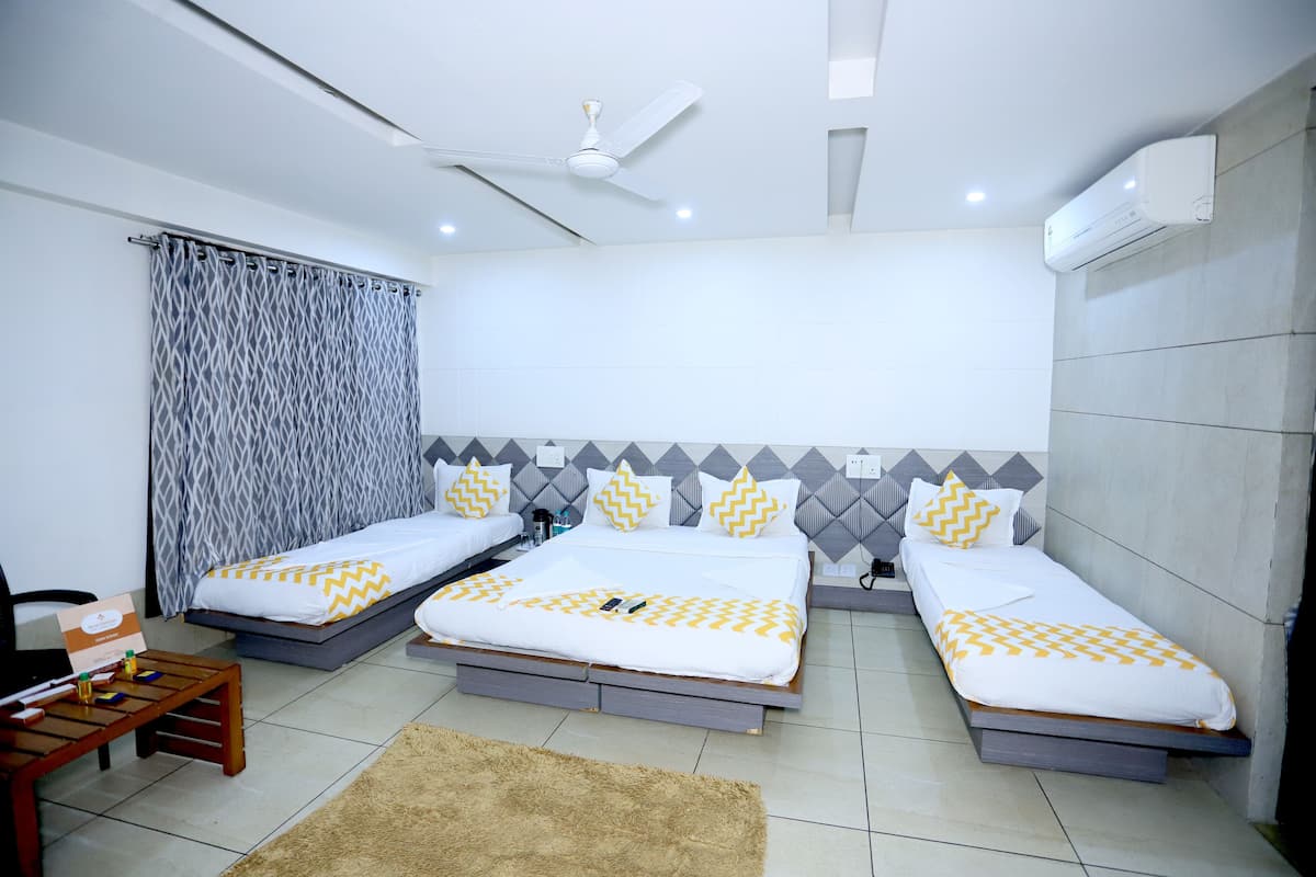 Quarto de hotel moderno com duas camas de solteiro, ventilador de teto, ar condicionado e uma pequena mesa de madeira.