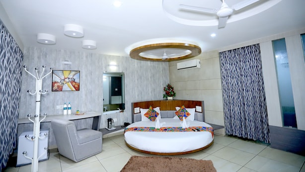 A modern bedroom with a round bed, a ceiling fan, a coat rack, and a bathroom with a shower and toilet. - Hotel darshan naroda (Ahmedabad)