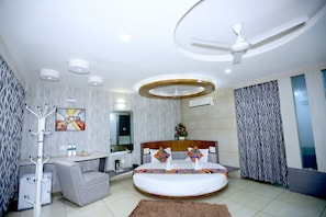Un dormitorio moderno con cama redonda, ventilador de techo, perchero y baño con ducha e inodoro.