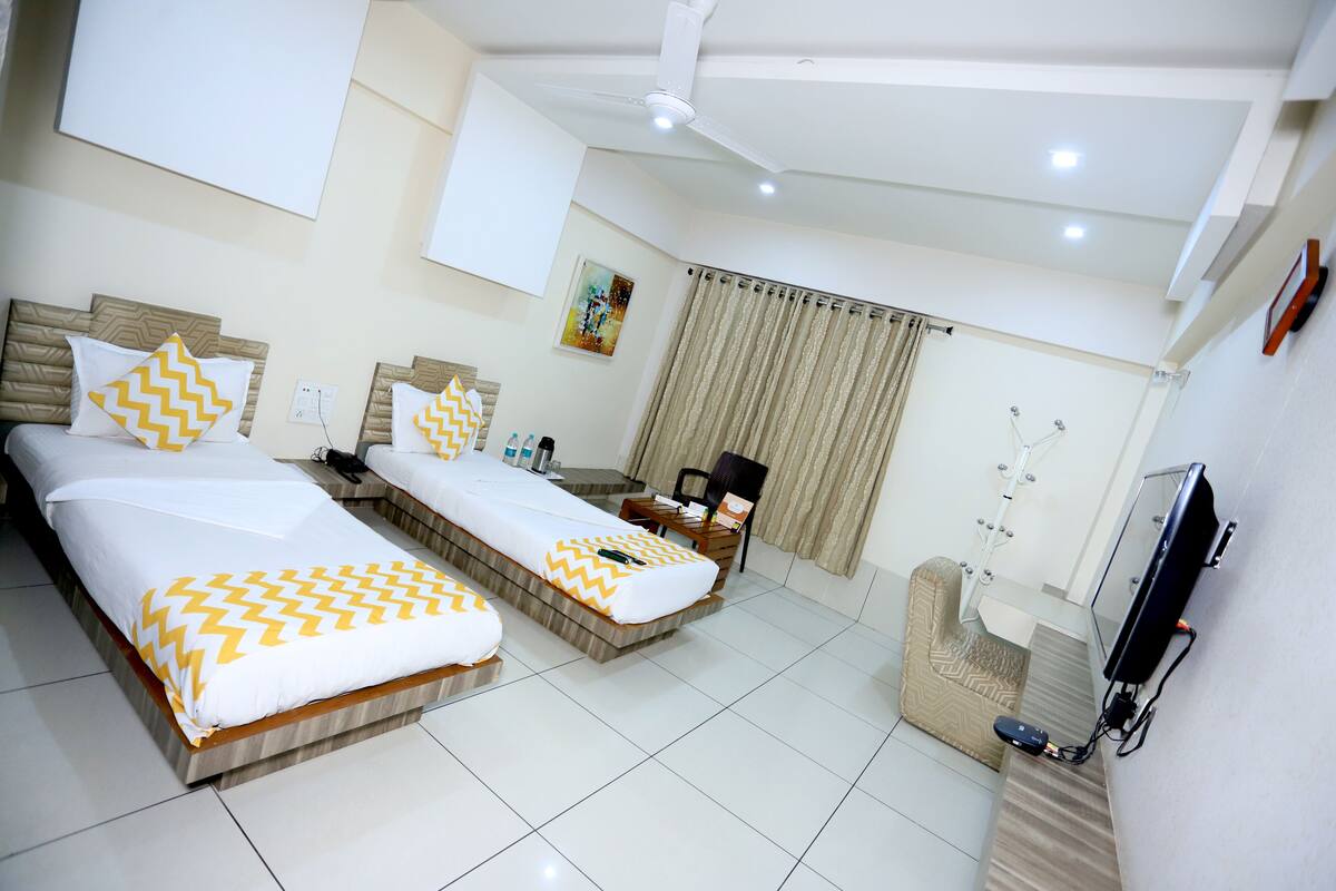 Quarto de hotel com duas camas, televisão, escrivaninha, cadeira e janela com cortinas.