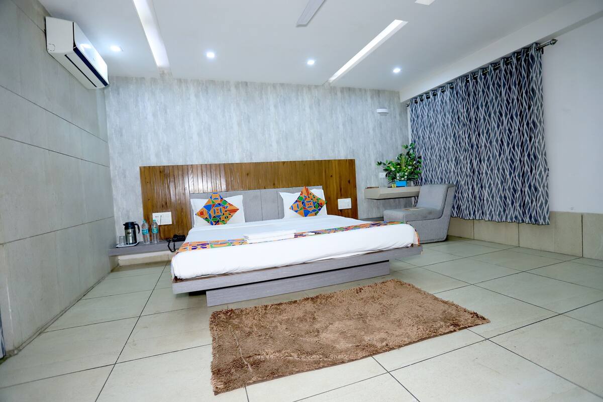 Quarto moderno com uma cama grande, mesas de cabeceira, máquina de café e cortina estampada.