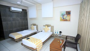 A hotel room with two single beds, a wooden coffee table, a chair, a desk, and an air conditioning unit. - Hotel darshan naroda (Ahmedabad)