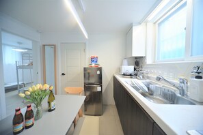 A modern kitchen with a stainless steel refrigerator, a sink with a dish rack, and a vase with flowers on the counter. - Jerry Blossom - Hostel (Seoul)