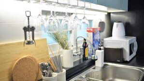 A kitchen with a stainless steel sink, a microwave, and a wine glass rack above the counter. - Jerry Blossom - Hostel (Seoul)
