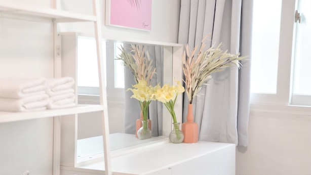 A white vanity with a mirror, two vases with yellow flowers, and a shelf with folded towels. - Jerry Blossom - Hostel (Seoul)