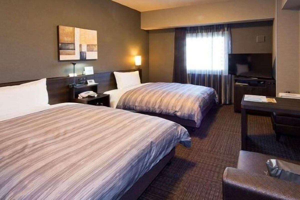 Een hotelkamer met twee bedden, een bureau, een stoel, een televisie en een raam met gordijnen.