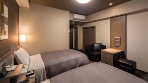 Une chambre d’hôtel avec deux lits, un bureau avec un ordinateur, une chaise et une petite table.