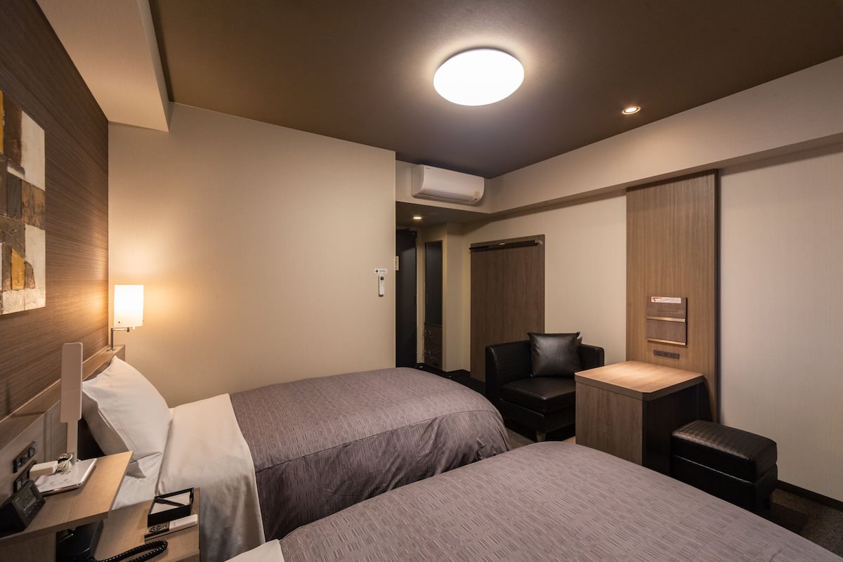 A hotel room with two beds, a desk with a computer, a chair, and a small table.