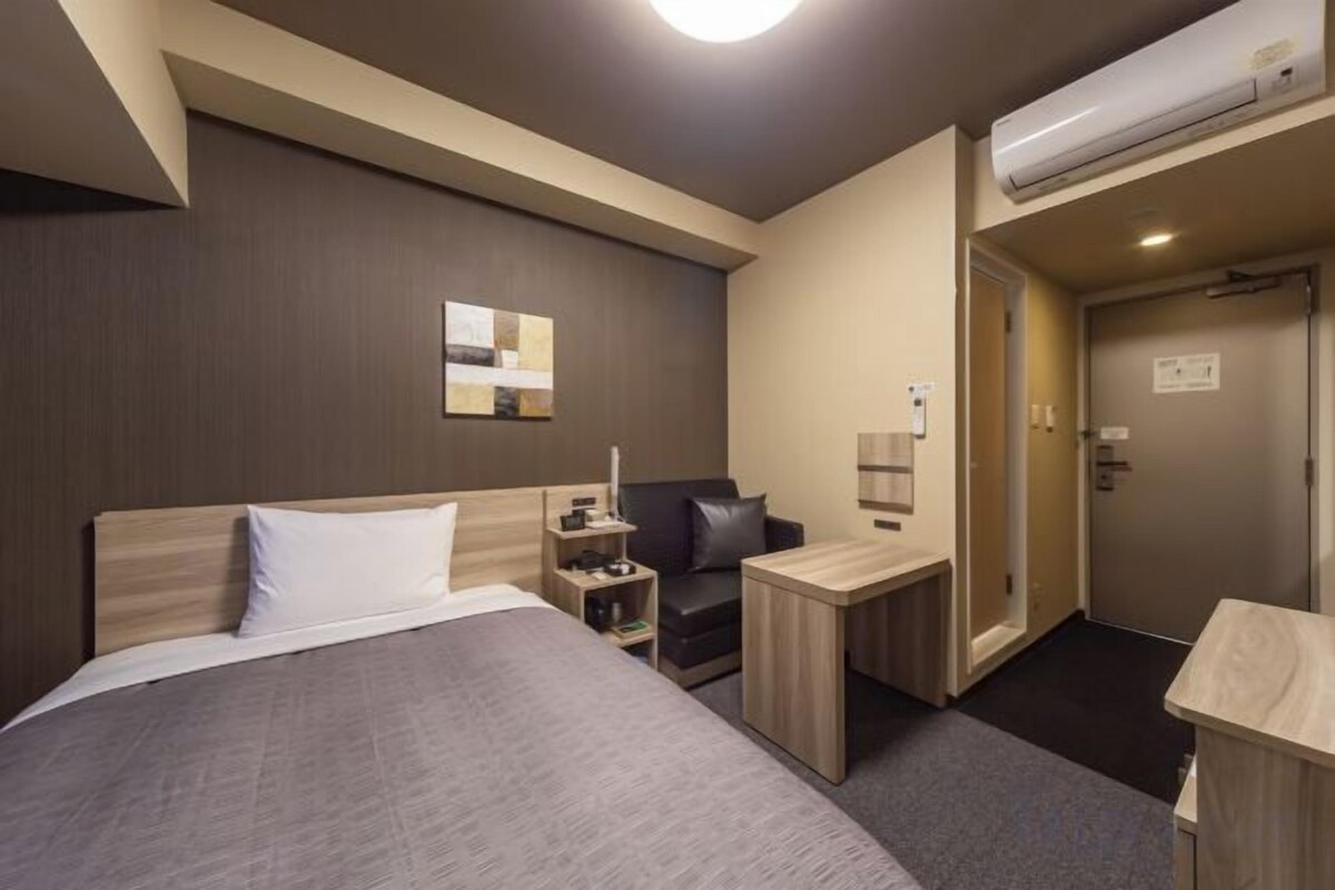 Een hotelkamer met een bed, bureau, stoel, nachtkastje en een kledingkast.