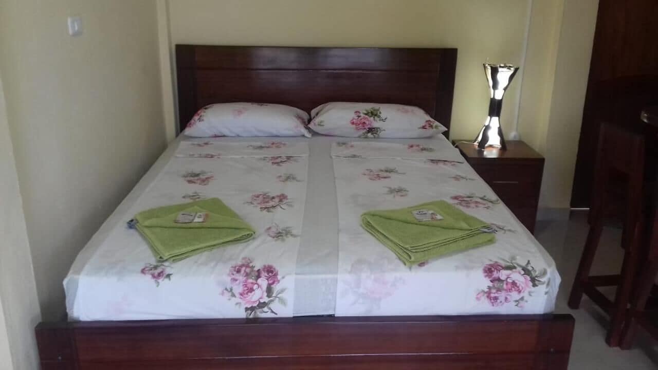 A double bed with floral bedding, two pillows, a bedside table with a lamp, and a wooden nightstand.
